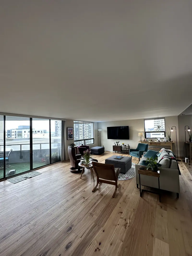 Furnished condo living room with a wide plank wood floor running to balcony doors and city views