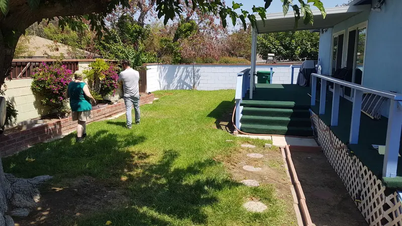 Back yard grass lawn beside a covered porch with a white railing before the work