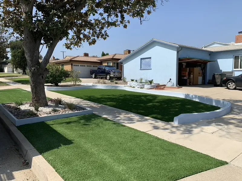 Front yard with artificial turf, curved concrete curbing and a gravel planting bed in front of a blue house