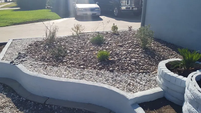 Gravel planting bed with low shrubs held by concrete curbing at the corner of the house