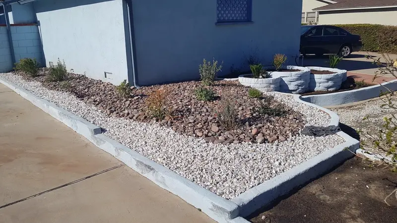 Bed of white and red rock with shrubs edged by concrete curbing along the house wall
