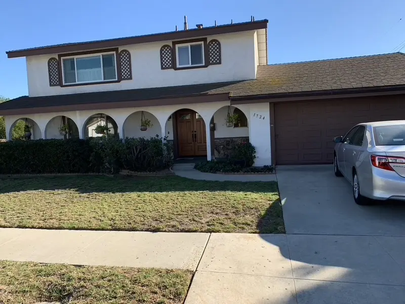 Two story stucco house with a front lawn and a concrete driveway before the pavers