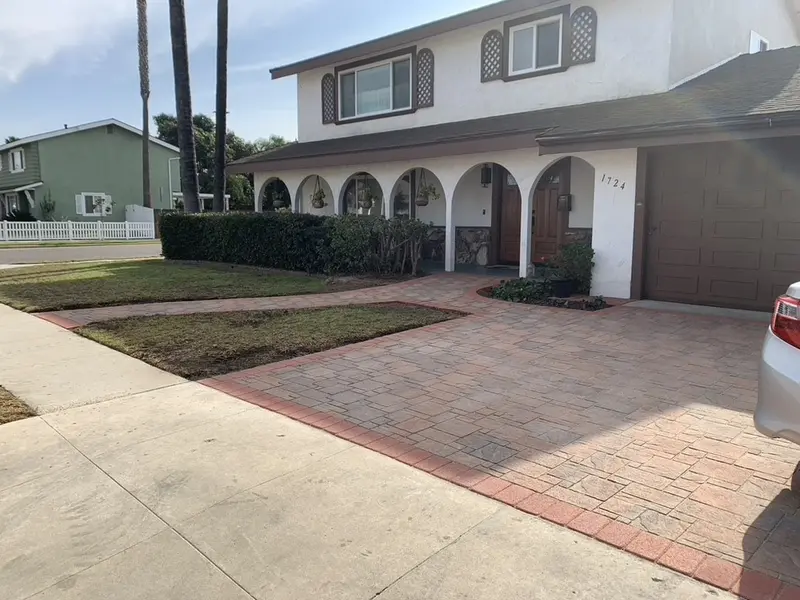 Reddish paver apron with a darker red border running beside a concrete driveway in front of a two story house