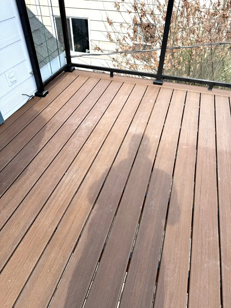 Close view of brown composite deck boards running to black-framed glass railing panels
