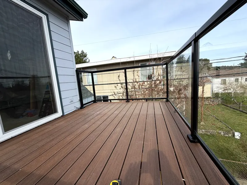 Corner of an upper deck where the glass railing meets the house wall beside a large window