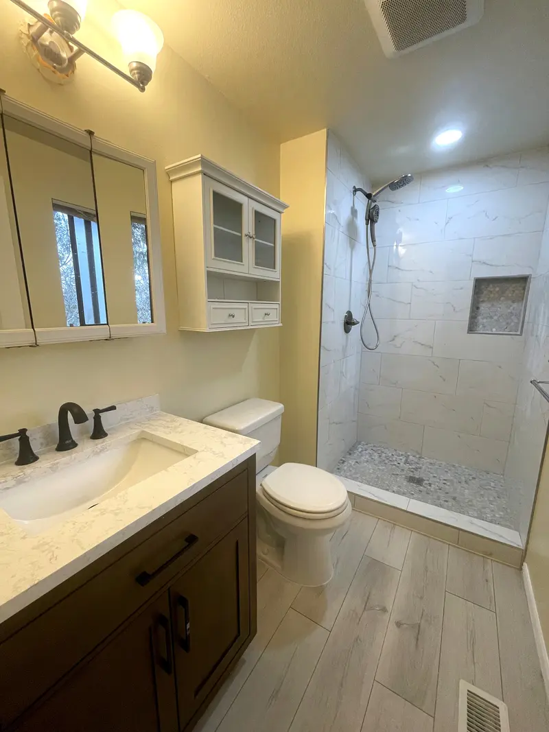 Guest bathroom with a dark wood vanity and light stone-look top beside a walk-in shower in marble-look tile