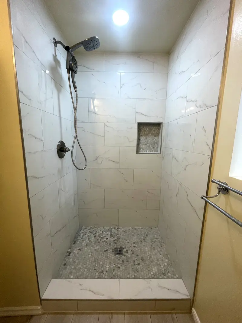 Straight-on view of the walk-in shower with a pebble-backed niche and a marble-look tile curb