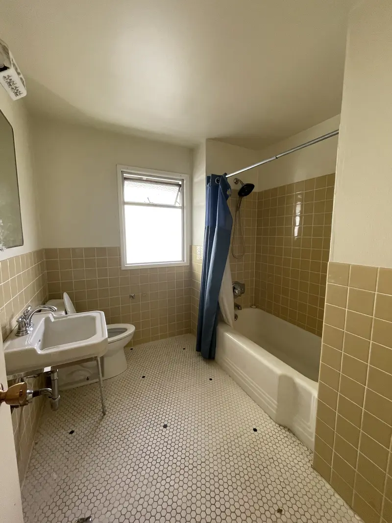Guest bathroom with a pedestal sink, tub and tan wainscot tile before the remodel