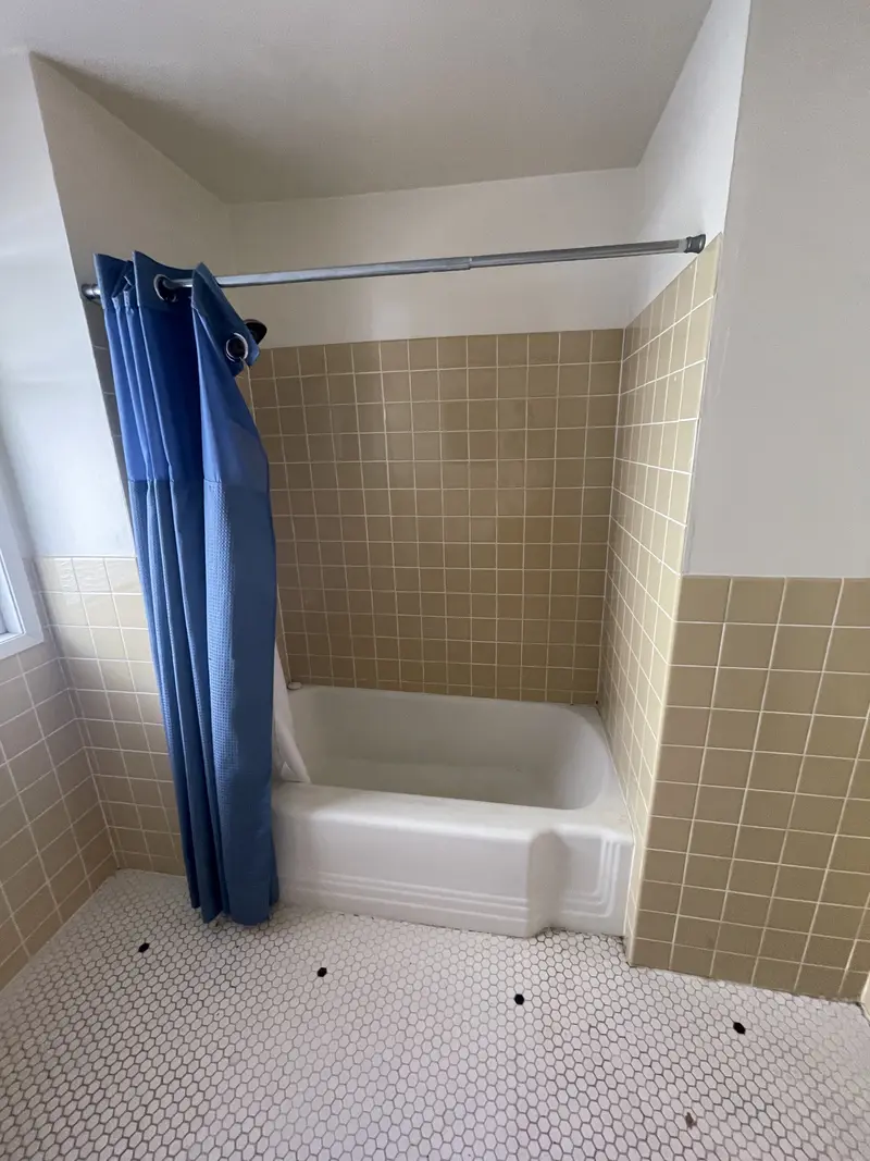 Old tub alcove with tan tile walls and a white penny tile floor