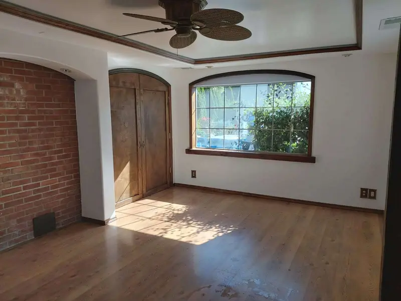 Brick alcove, wood doors and the arched front window in a white bedroom with sunlight on the floor