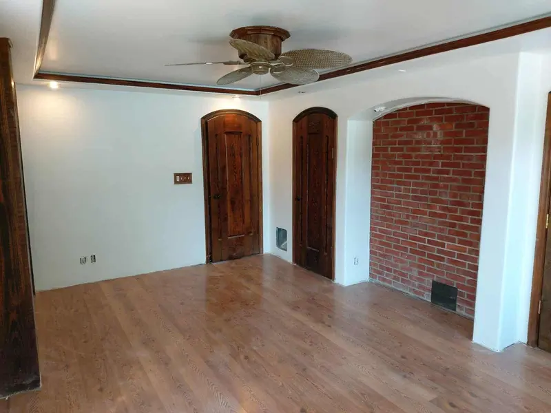 Finished white bedroom with a ceiling fan, two arched doors and a brick accent wall