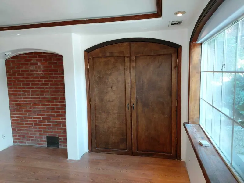 Exposed brick accent wall in an arched alcove beside arched wood double doors and a tall window