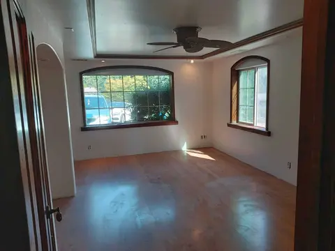 Bright white bedroom with an arched front window, stained trim, a coffered ceiling and a wood floor