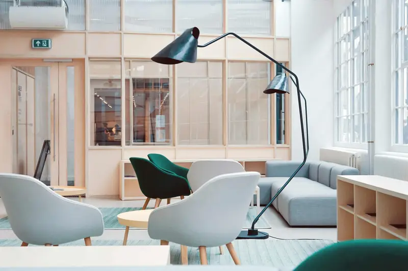 Bright lounge with gray and green armchairs, a blue sofa, a black floor lamp and tall windows