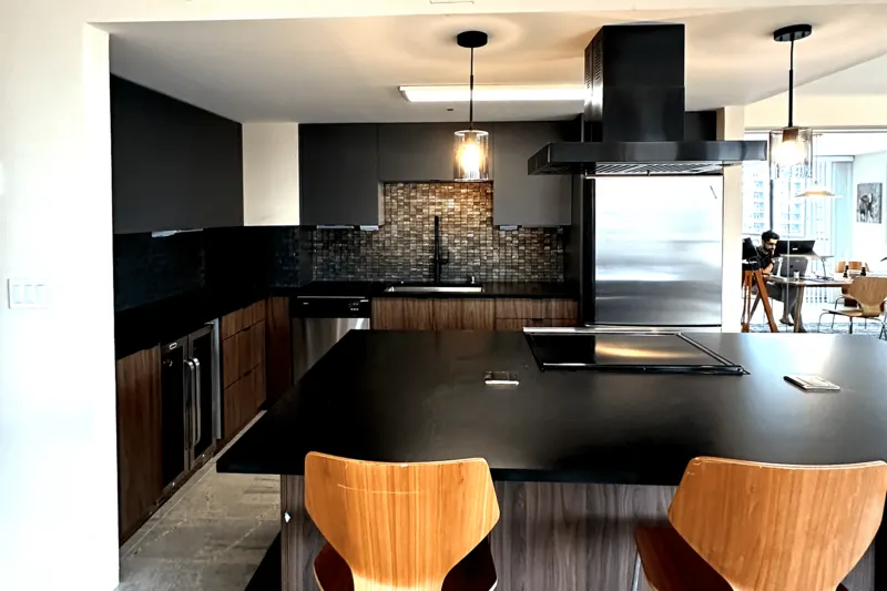 Remodeled condo kitchen in Seattle, WA with a black island, walnut cabinets, a mosaic backsplash and pendant lights