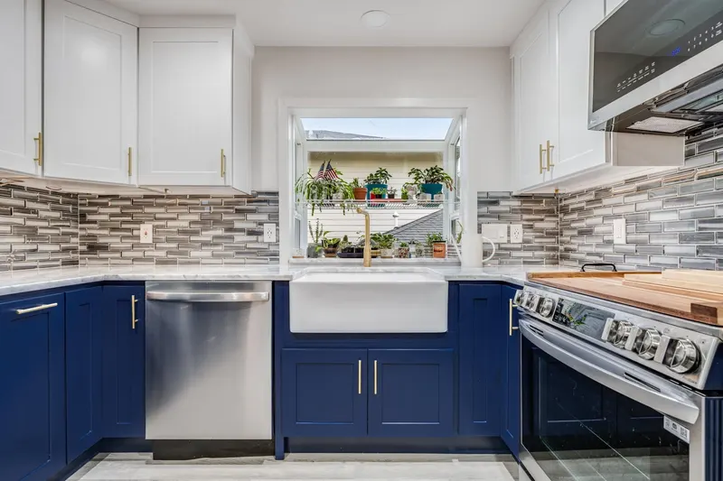 Remodeled kitchen in Lynnwood, WA with navy lower cabinets, white upper cabinets and a farmhouse sink under the window