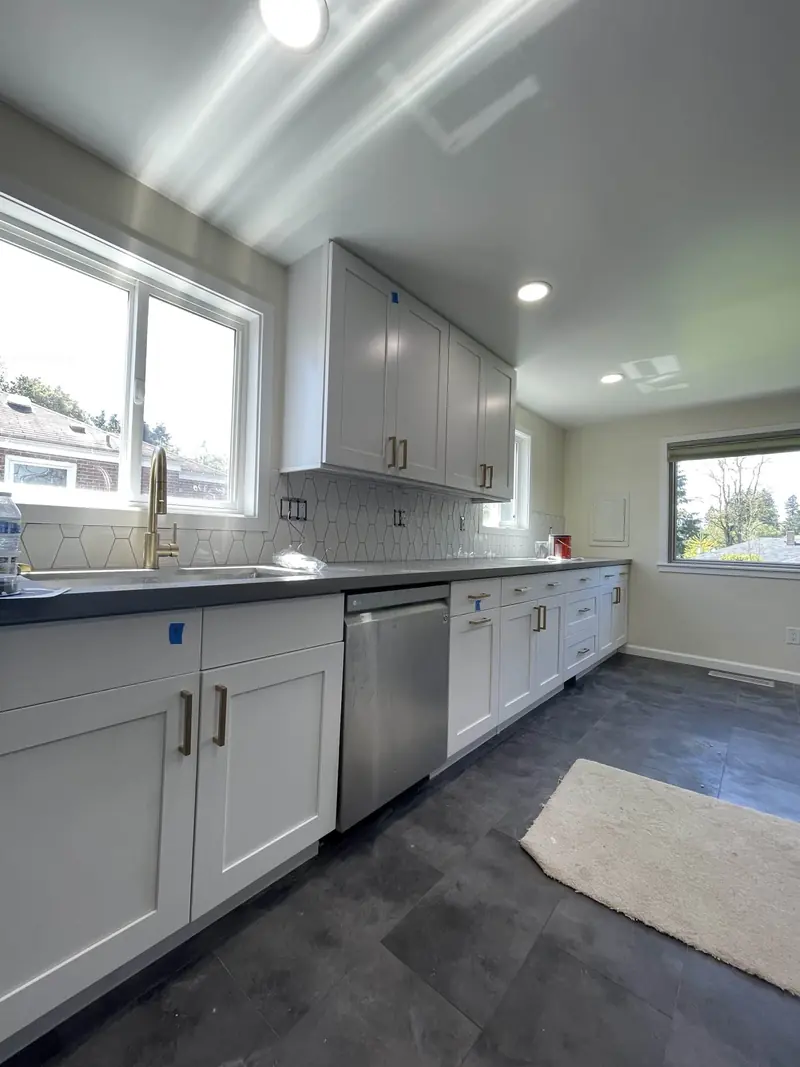 Kitchen sink wall with a brushed gold faucet, stainless dishwasher and white shaker cabinets