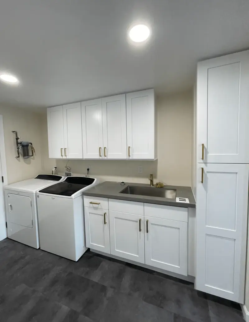 Remodeled laundry room with a washer, dryer, utility sink and white upper cabinets
