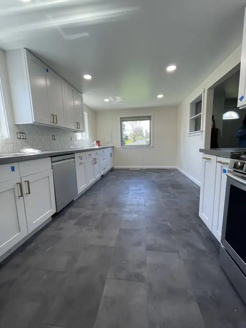 Remodeled galley kitchen with white shaker cabinets, gray quartz counters and a slate-look floor