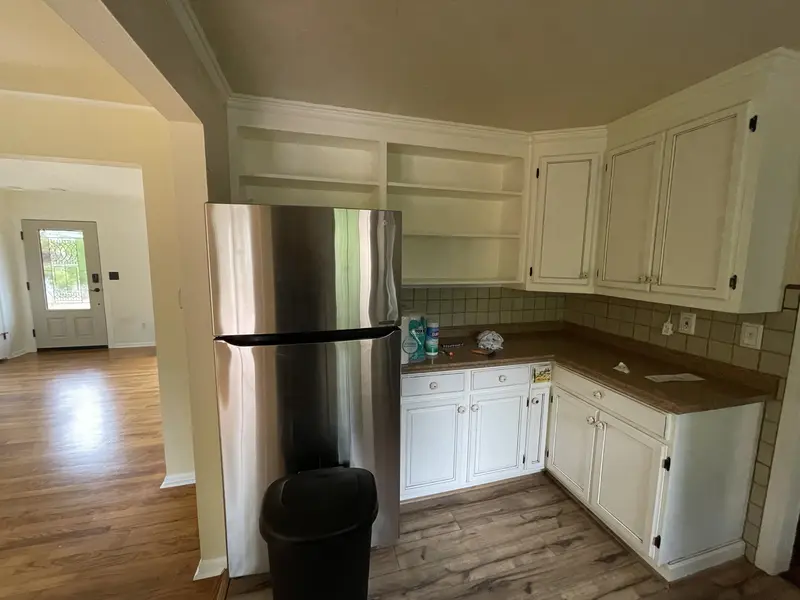 Corner of the old kitchen with a stainless refrigerator, open upper shelves and a doorway to the next room