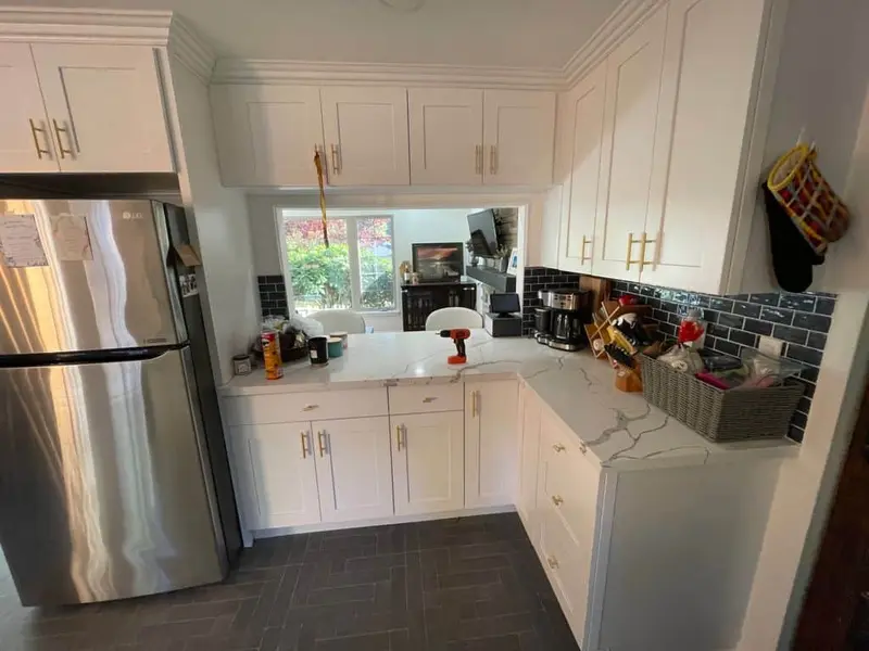 Kitchen corner with white shaker cabinets, gold pulls, marble-look counters and a pass-through to the dining room
