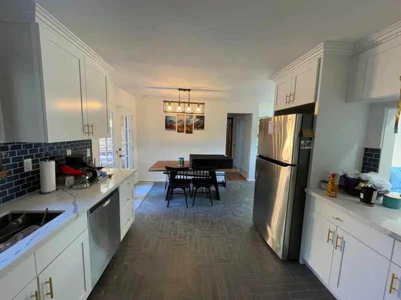 Finished kitchen with white shaker cabinets, a navy subway tile backsplash and a charcoal herringbone floor leading to the dining table
