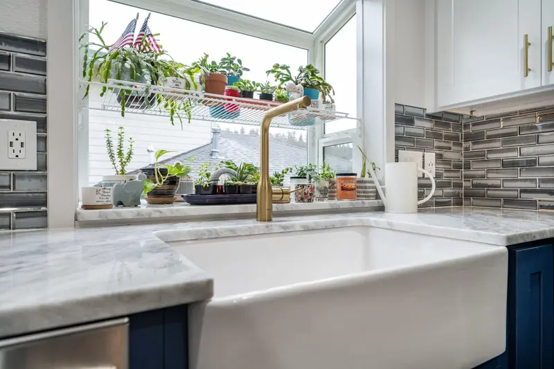 Close view of a white ceramic farmhouse sink, a gold faucet and a veined quartzite counter