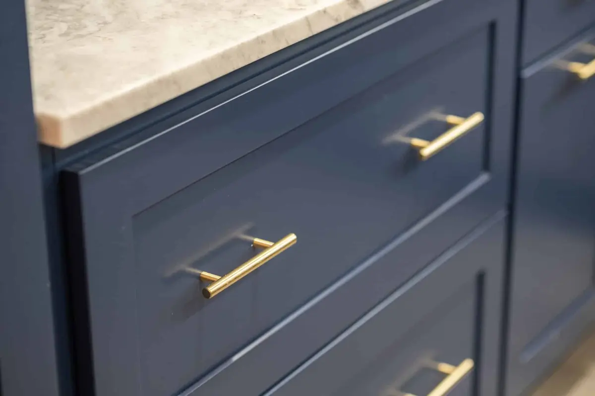 Navy shaker drawer fronts with satin brass bar pulls under a quartzite counter edge