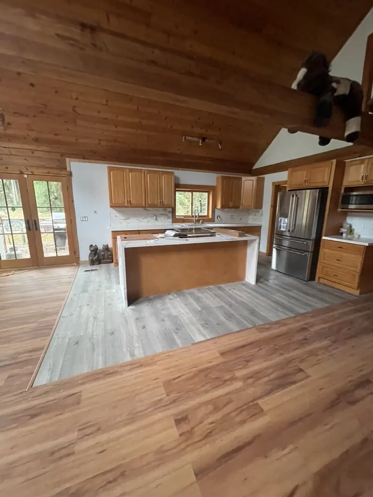 Kitchen island on a light gray plank floor framed by a warm wood-look floor