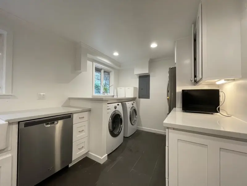 Stainless dishwasher in a white cabinet run leading to the laundry nook