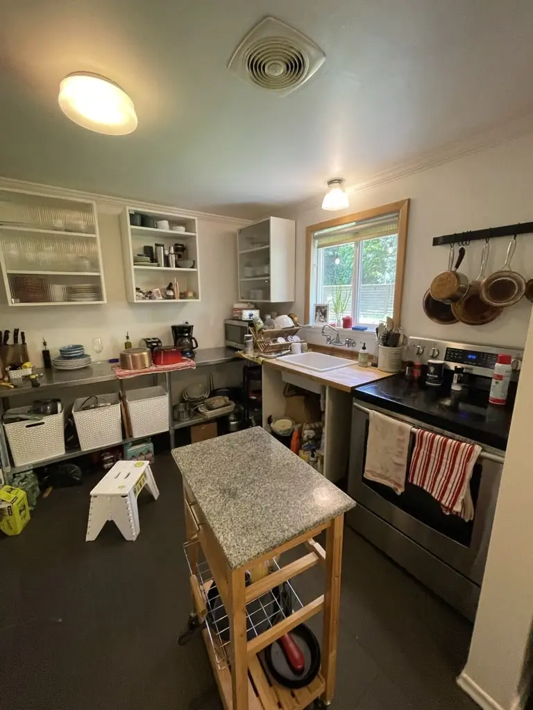 Old kitchen range wall with hanging pans, open shelves and a granite-topped cart