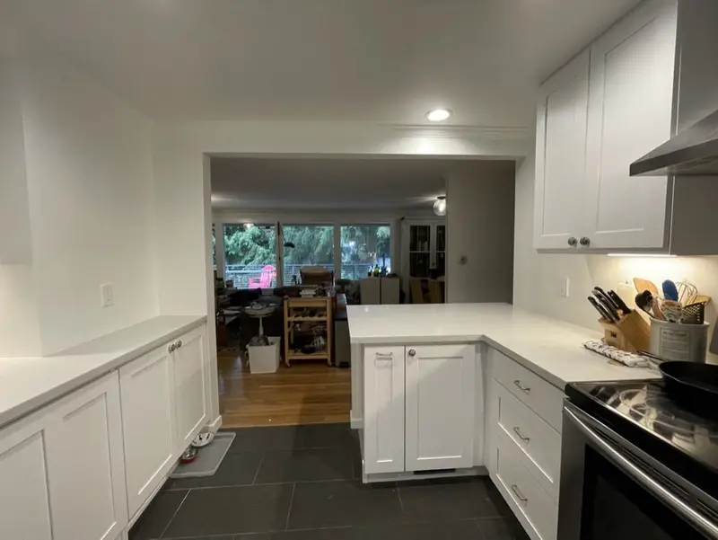 White kitchen looking out through a wide opening to a living room with a wood floor