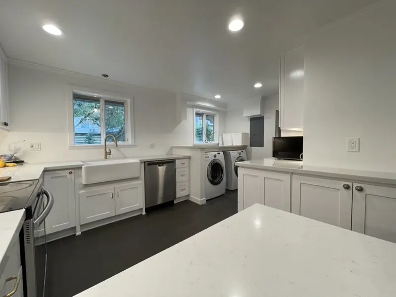 White farmhouse sink and dishwasher under two windows, with the laundry nook at the end of the run
