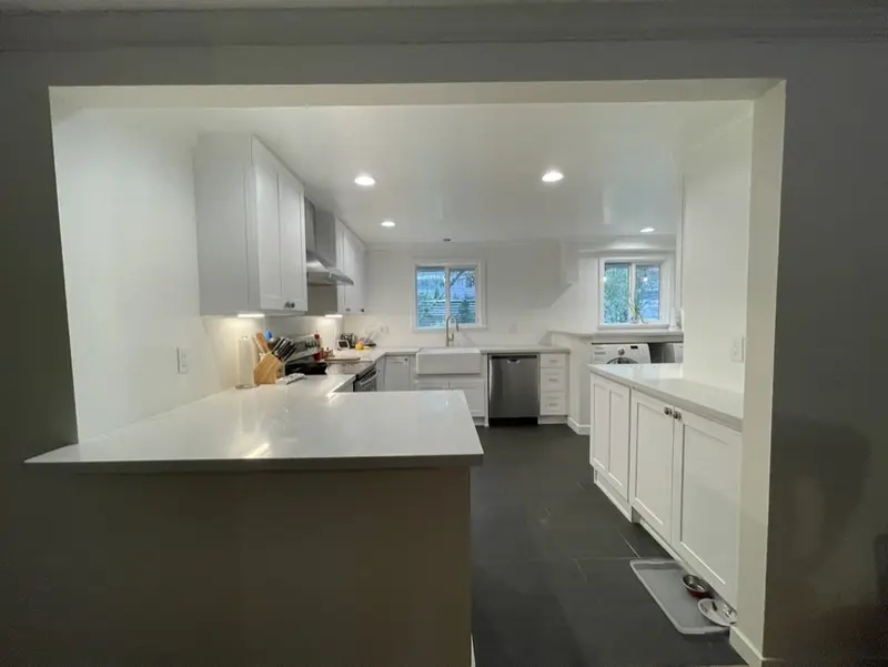 Wide opening framed into a white kitchen, seen from the next room, with the peninsula in front