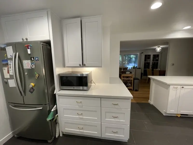 French door refrigerator beside tall white cabinets with a microwave on the counter