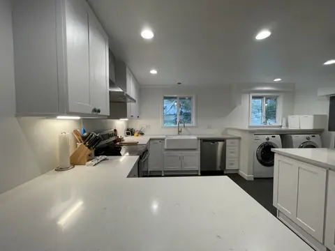 Remodeled white shaker kitchen with a white peninsula counter, a farmhouse sink under the windows and recessed lights
