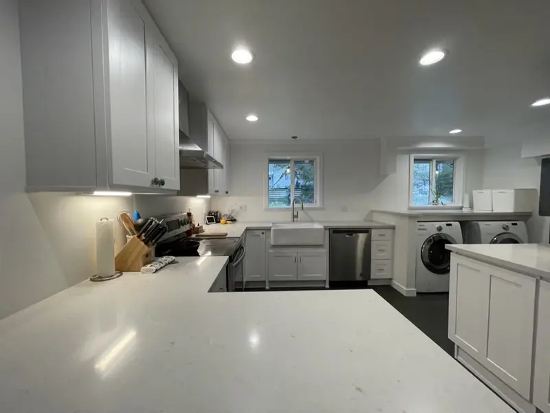 Remodeled white shaker kitchen with a white peninsula counter, a farmhouse sink under the windows and recessed lights