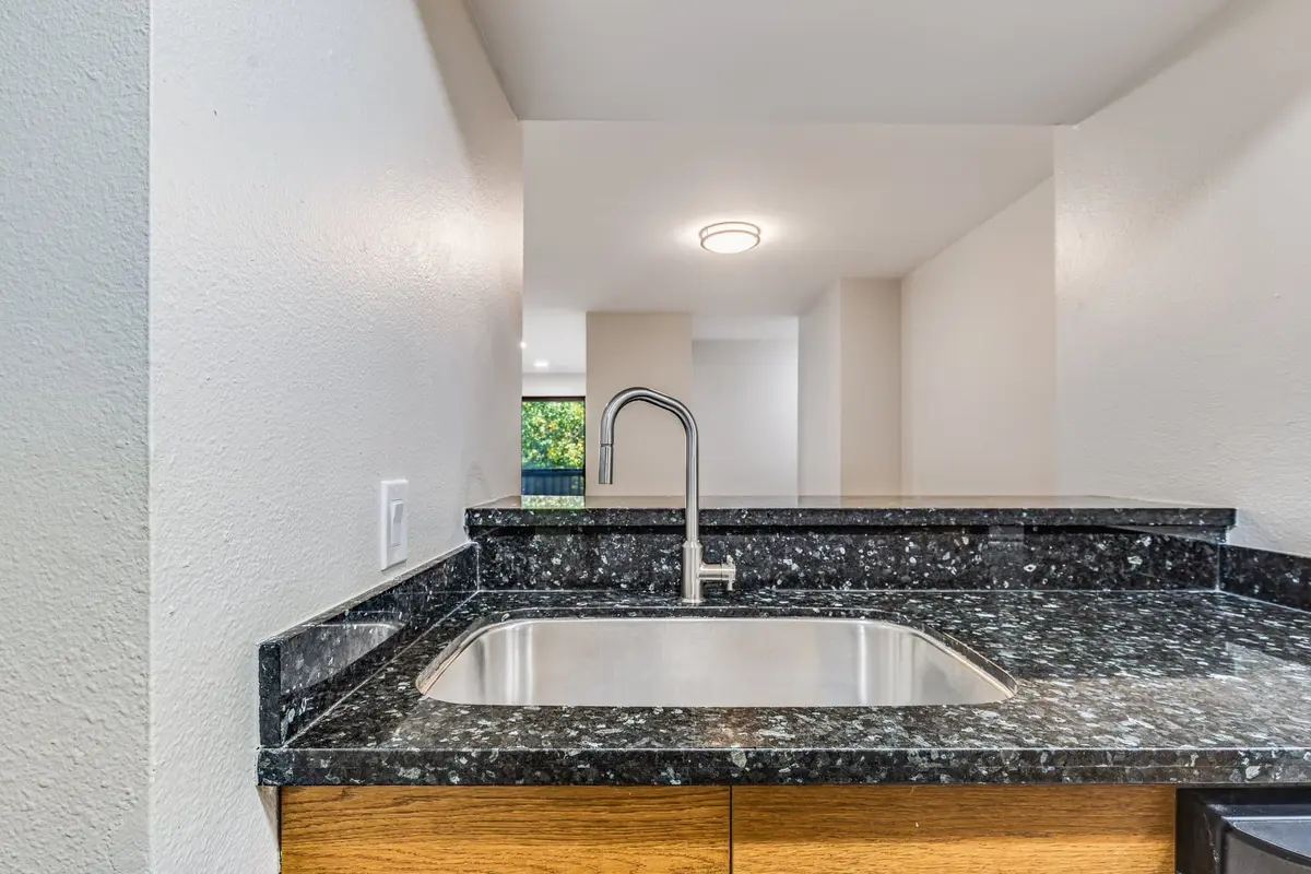 Stainless undermount sink in a dark speckled granite counter below a kitchen pass-through