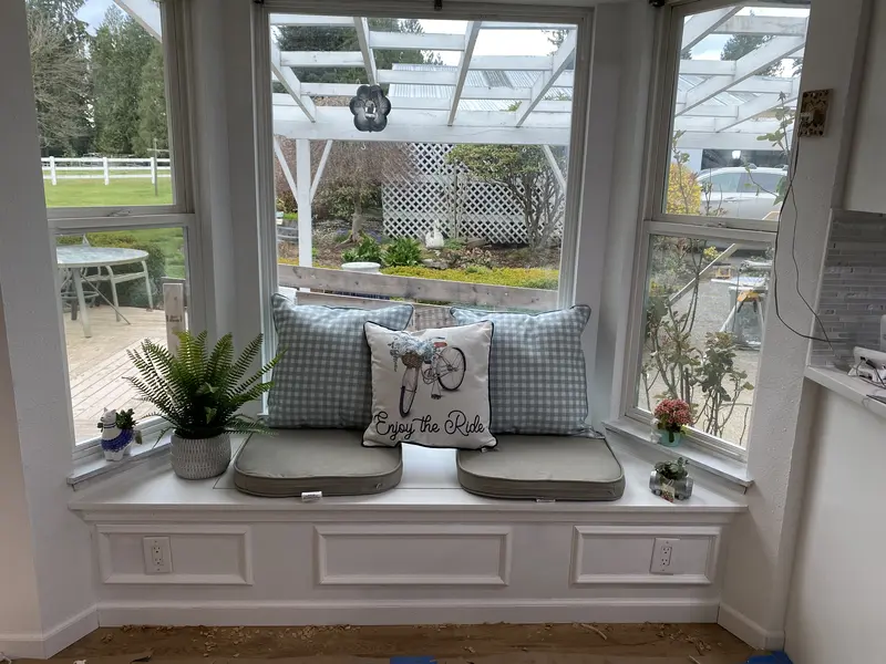 Finished bay window seat with cushions and pillows, looking out to the yard