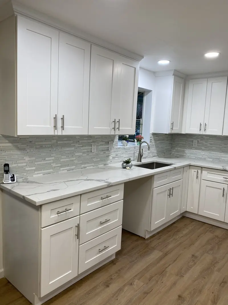 Corner of the white kitchen with tall cabinets and a warm wood-look plank floor