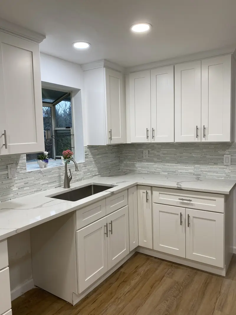 L-shaped white kitchen with drawers, a corner sink run and a gray glass tile backsplash