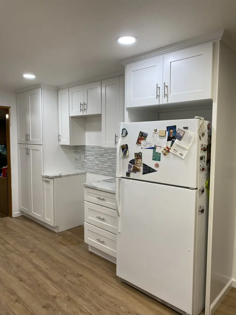 Wall of tall white pantry cabinets around the refrigerator, with recessed lights above
