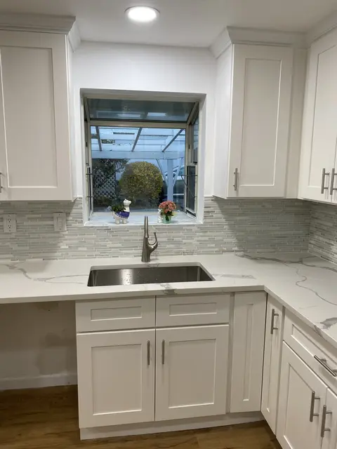 White shaker kitchen with a stainless sink under a window and a gray glass mosaic backsplash