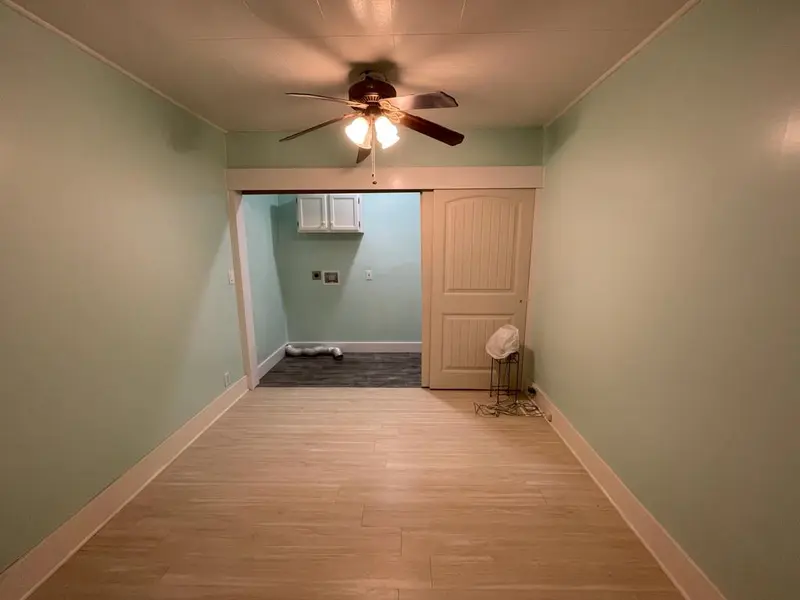 Long room with a light plank floor and mint walls, a sliding door open on a laundry alcove with upper cabinets