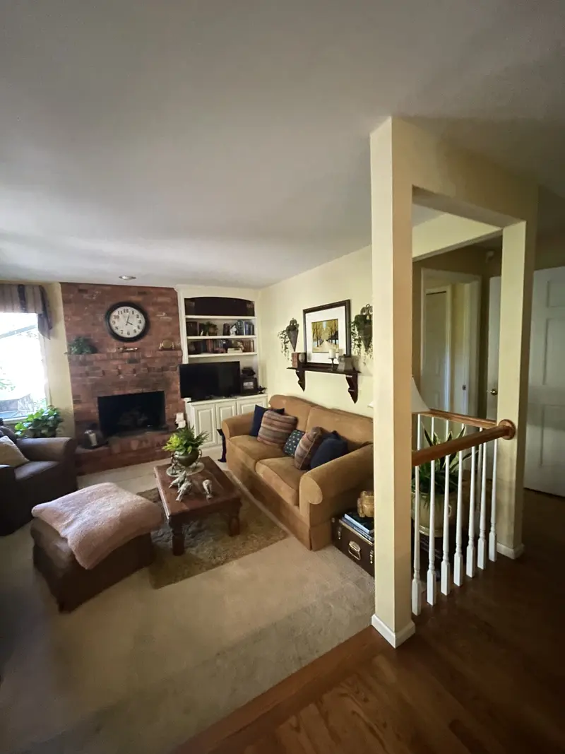 Living room with the red brick fireplace, a square post and a stair rail at the hall opening