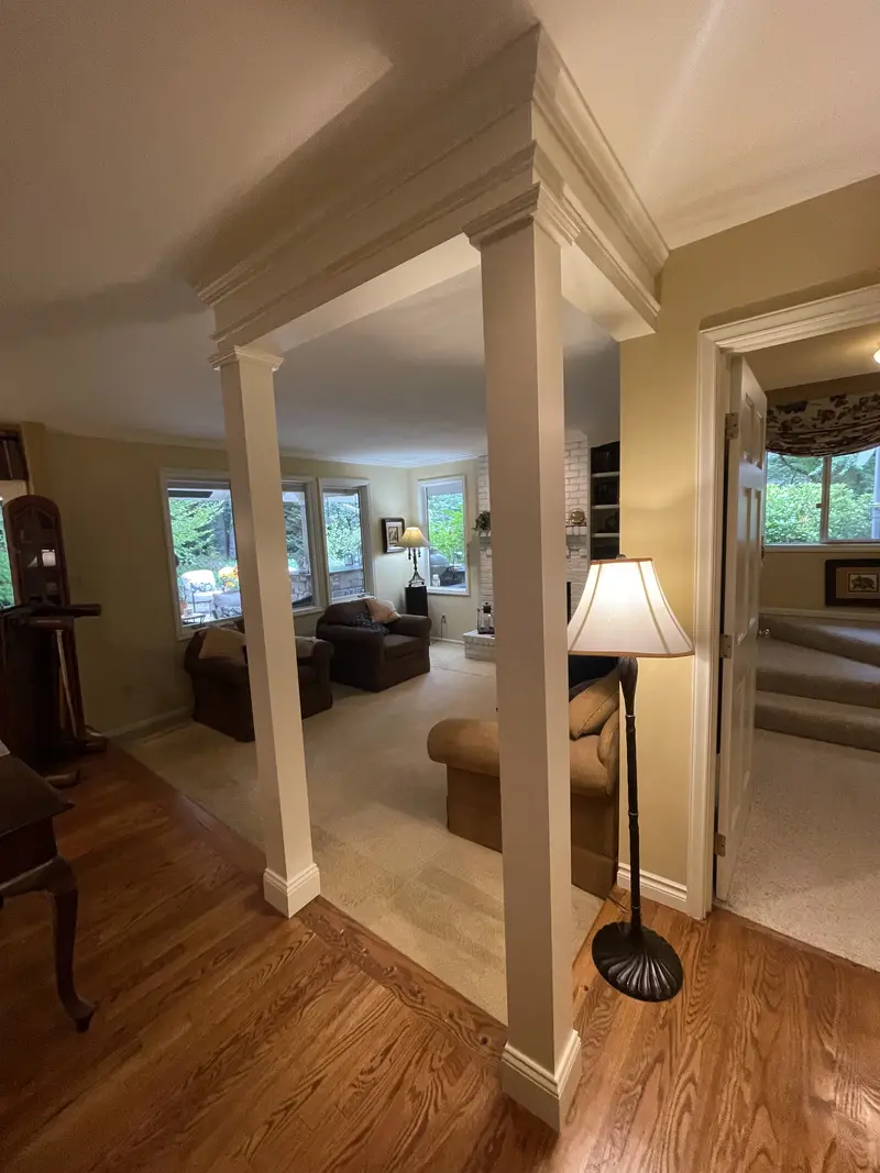Two square white columns with trimmed bases under a beam at the opening beside a floor lamp