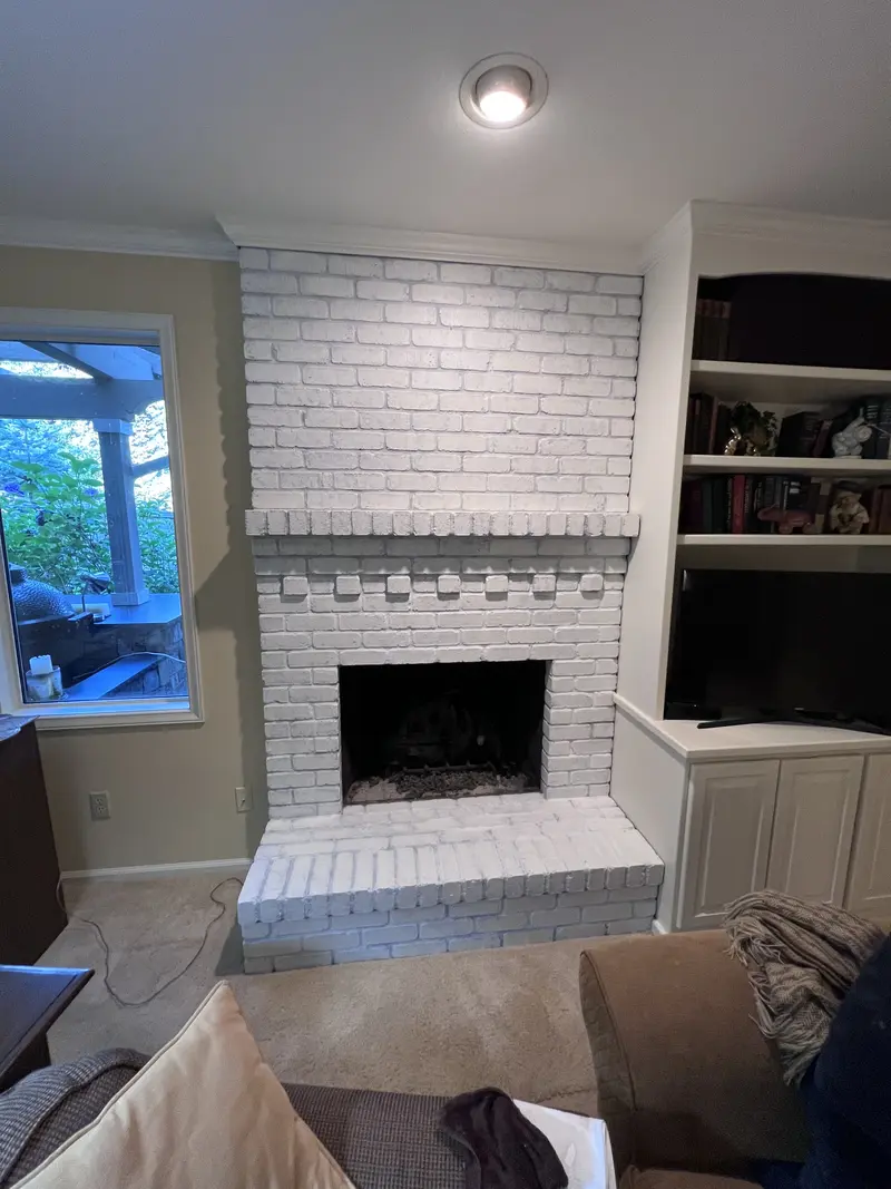 Close view of the white painted brick fireplace and raised hearth beside white built-in shelves