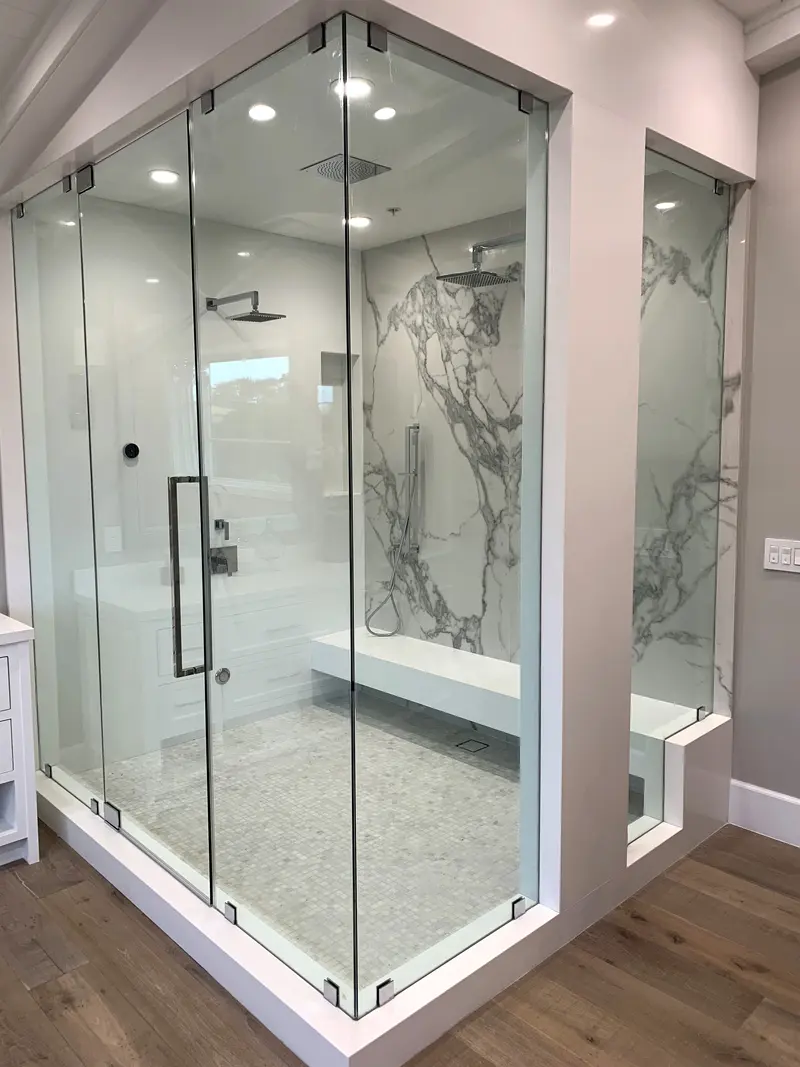 Walk-in shower enclosed in frameless glass with marble-look slab walls, a floating bench and a mosaic floor