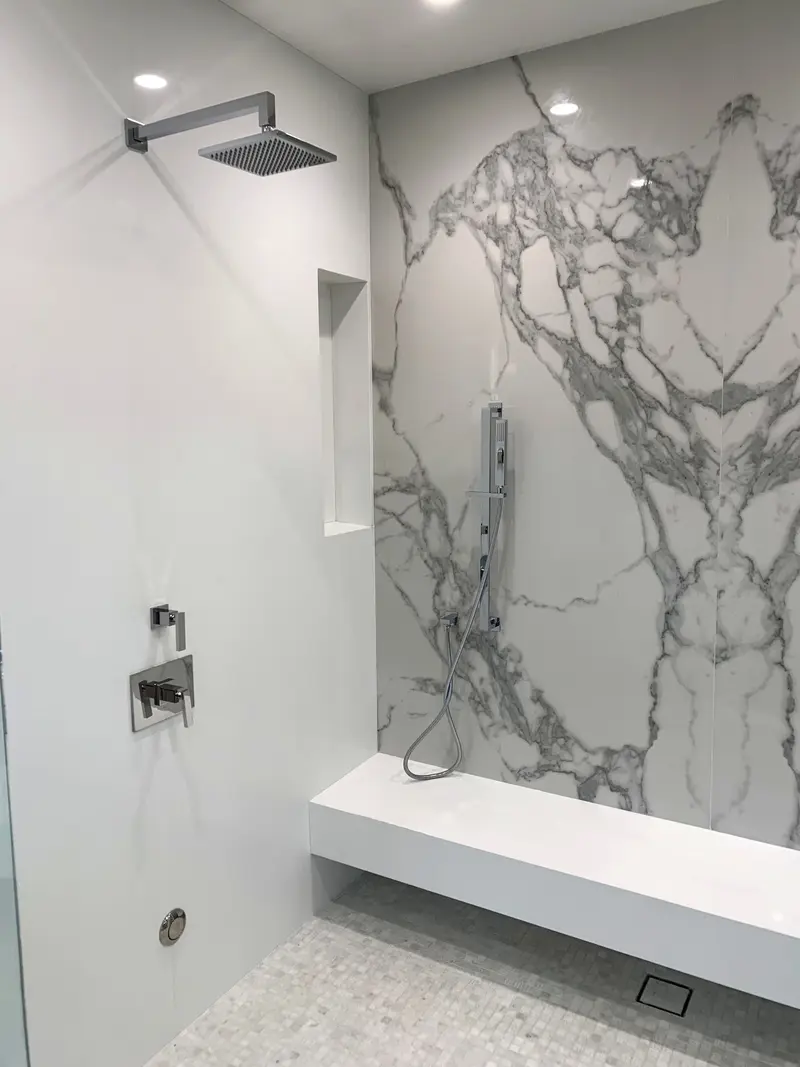 Inside the shower: a white floating bench against a marble-look slab wall, a square rain head and a handheld spray