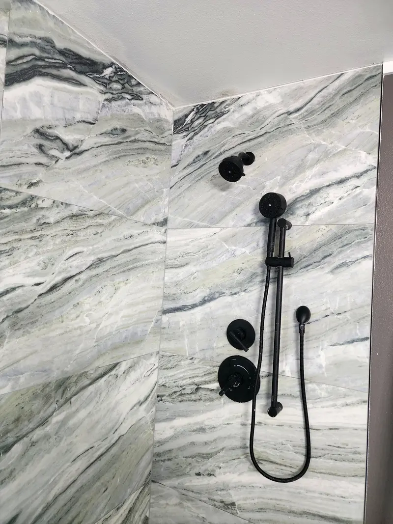 Matte black shower head, valve and handheld spray on a slide bar against large gray veined tile